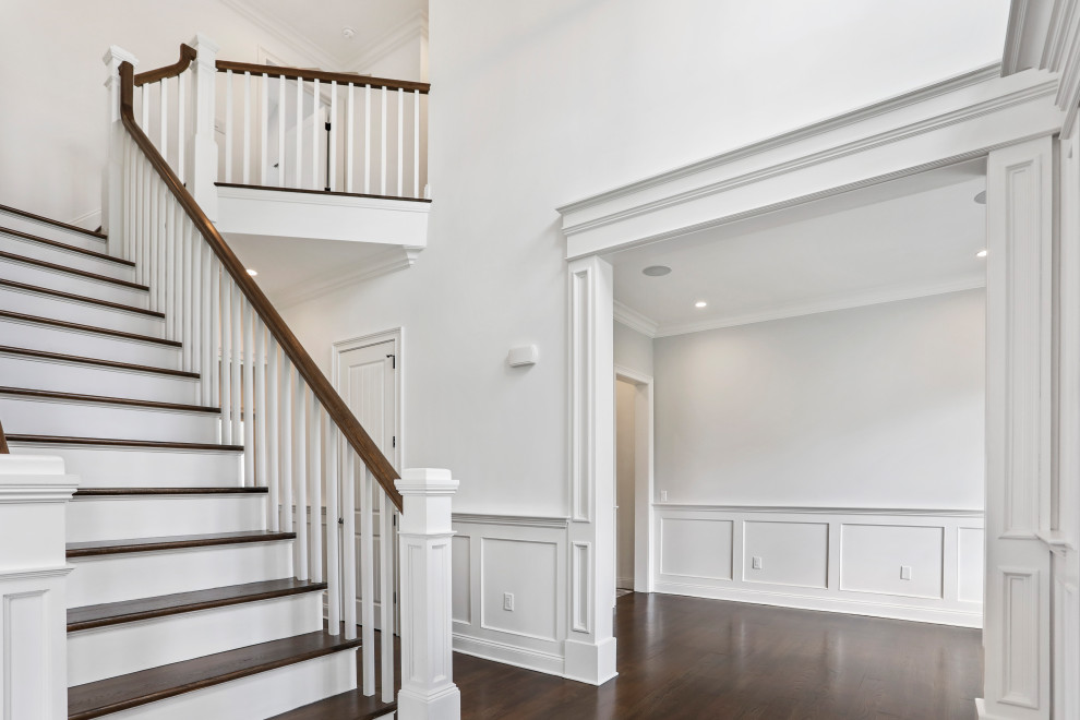 Großes Klassisches Foyer mit weißer Wandfarbe, dunklem Holzboden, Einzeltür, hellbrauner Holzhaustür, braunem Boden und vertäfelten Wänden in New York