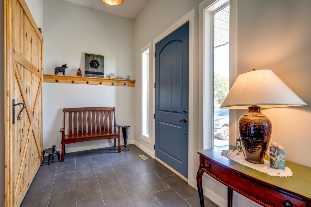 Idée de décoration pour une porte d'entrée champêtre de taille moyenne avec un mur gris, un sol en carrelage de porcelaine, une porte simple, une porte bleue et un sol marron.
