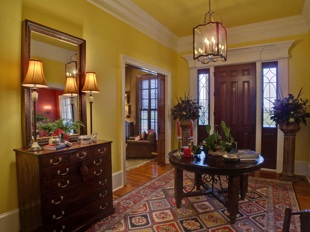 На фото: фойе среднего размера в классическом стиле с желтыми стенами, паркетным полом среднего тона, одностворчатой входной дверью и входной дверью из темного дерева