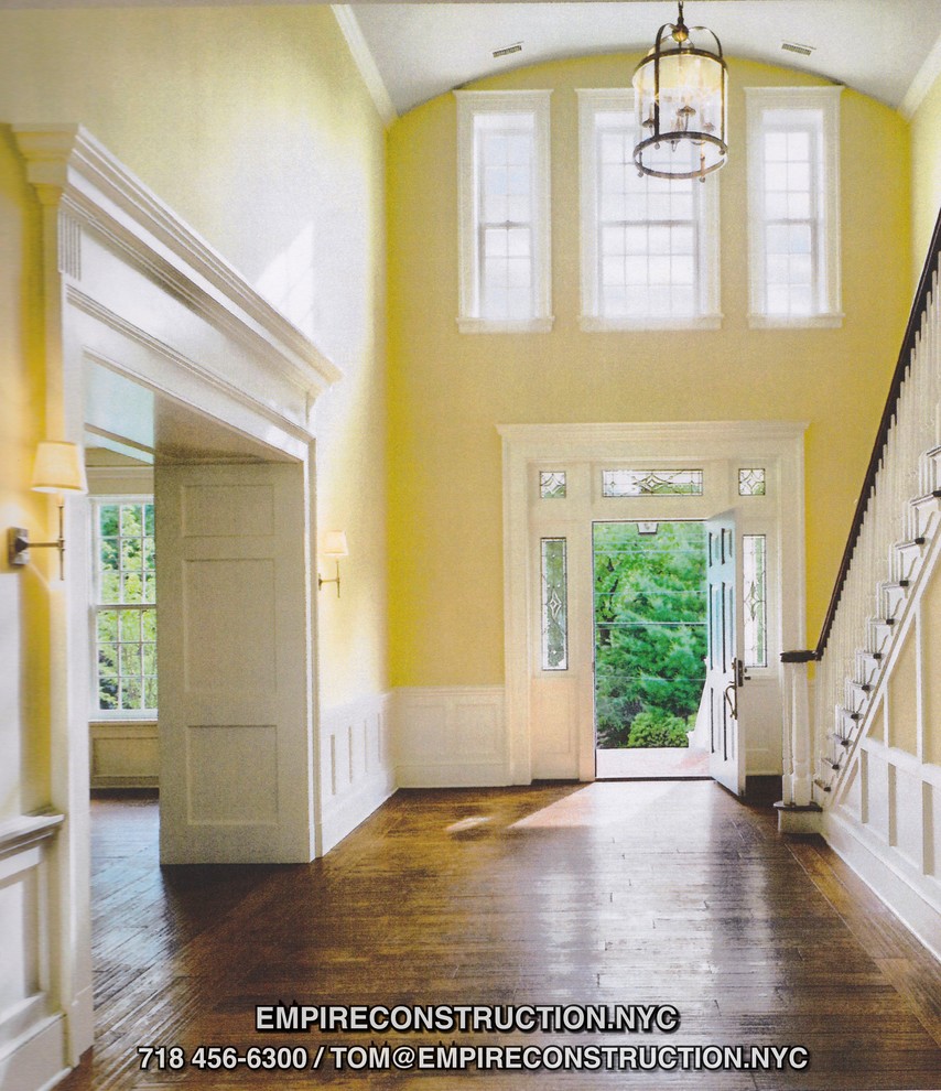 Cette photo montre une très grande entrée craftsman avec un couloir, un mur jaune, un sol en bois brun et une porte blanche.