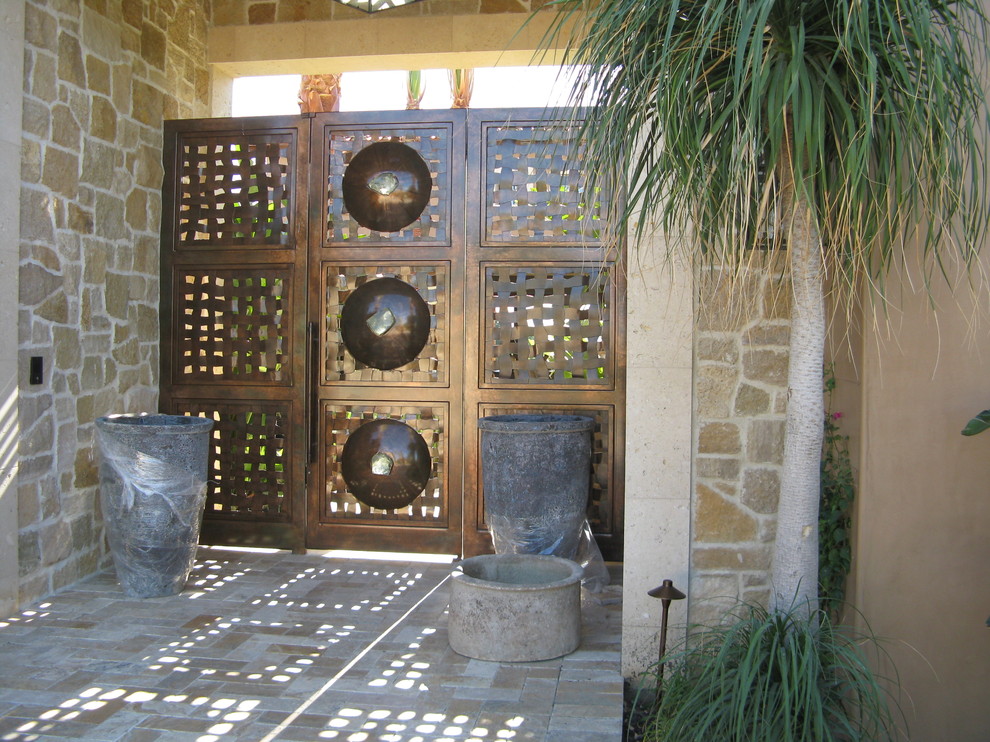 На фото: большая входная дверь в средиземноморском стиле с черными стенами, бетонным полом, поворотной входной дверью и металлической входной дверью с