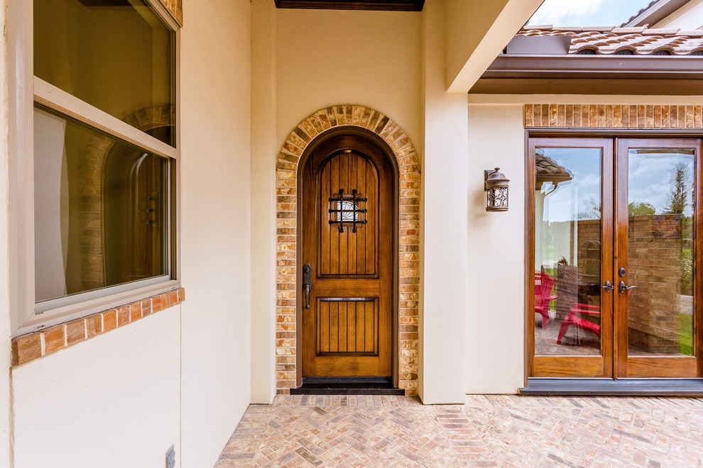 Foto de puerta principal mediterránea grande con paredes beige, suelo de ladrillo, puerta simple, puerta de madera en tonos medios y suelo beige