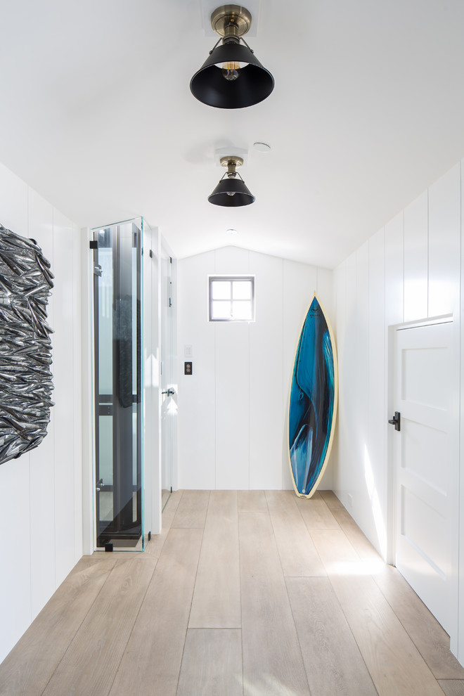 This is an example of a beach style hallway in Orange County with white walls, light hardwood flooring, beige floors and feature lighting.
