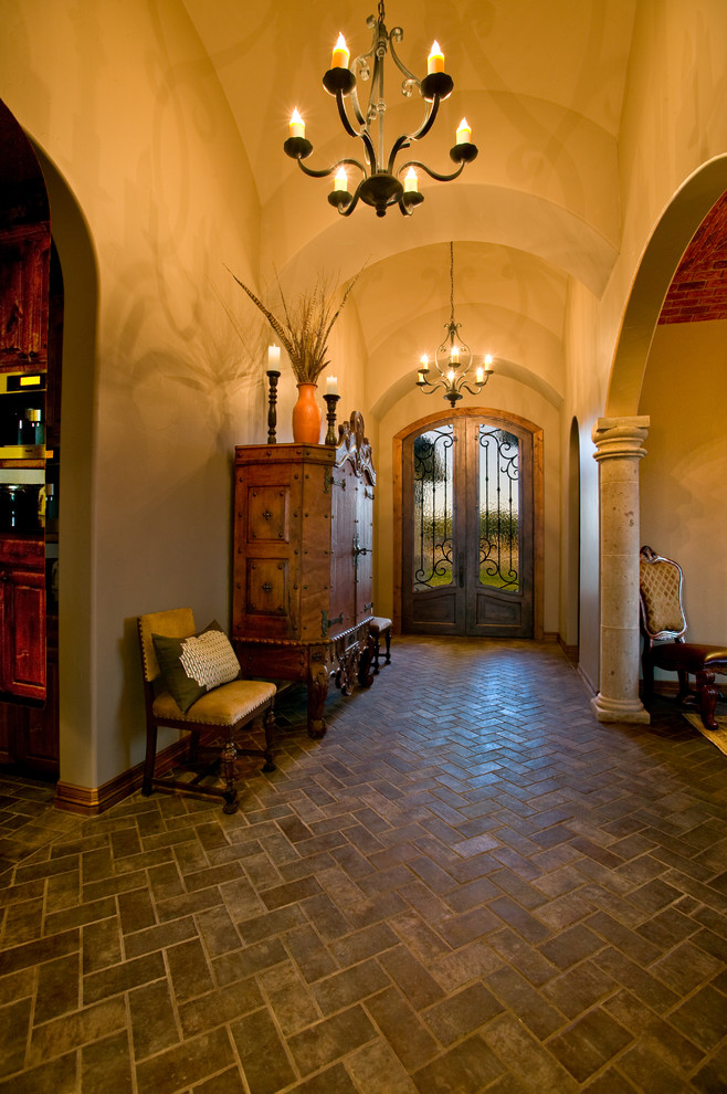 Photo of a large mediterranean foyer in Austin with beige walls, brick flooring, a double front door, a glass front door and brown floors.