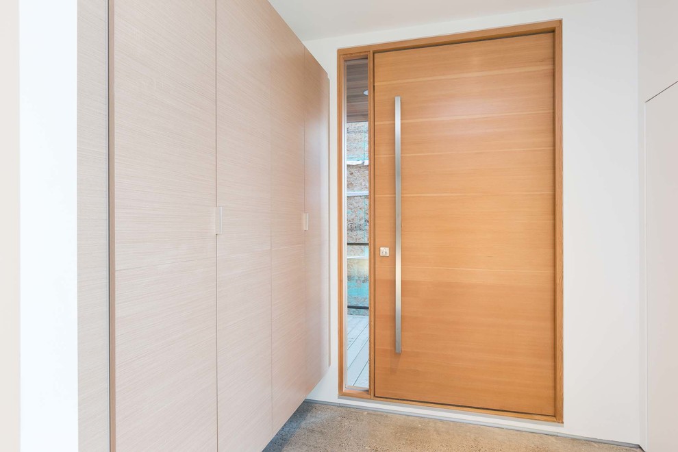 На фото: входная дверь среднего размера в стиле модернизм с белыми стенами, бетонным полом, поворотной входной дверью, входной дверью из дерева среднего тона и серым полом с