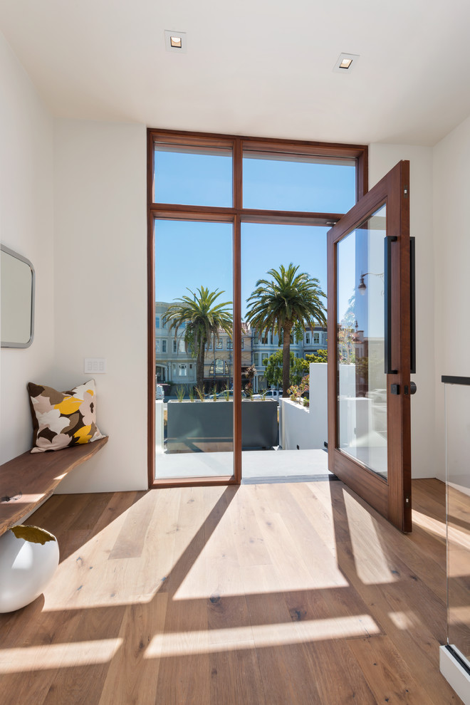 This is an example of a medium sized contemporary front door in San Francisco with white walls, light hardwood flooring, a pivot front door, a glass front door and beige floors.