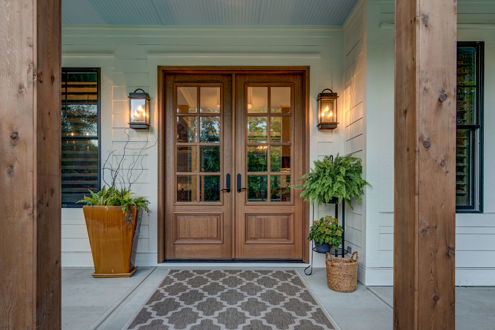 Cette image montre une porte d'entrée craftsman avec un mur beige, sol en béton ciré, une porte double, une porte en bois brun et un sol gris.