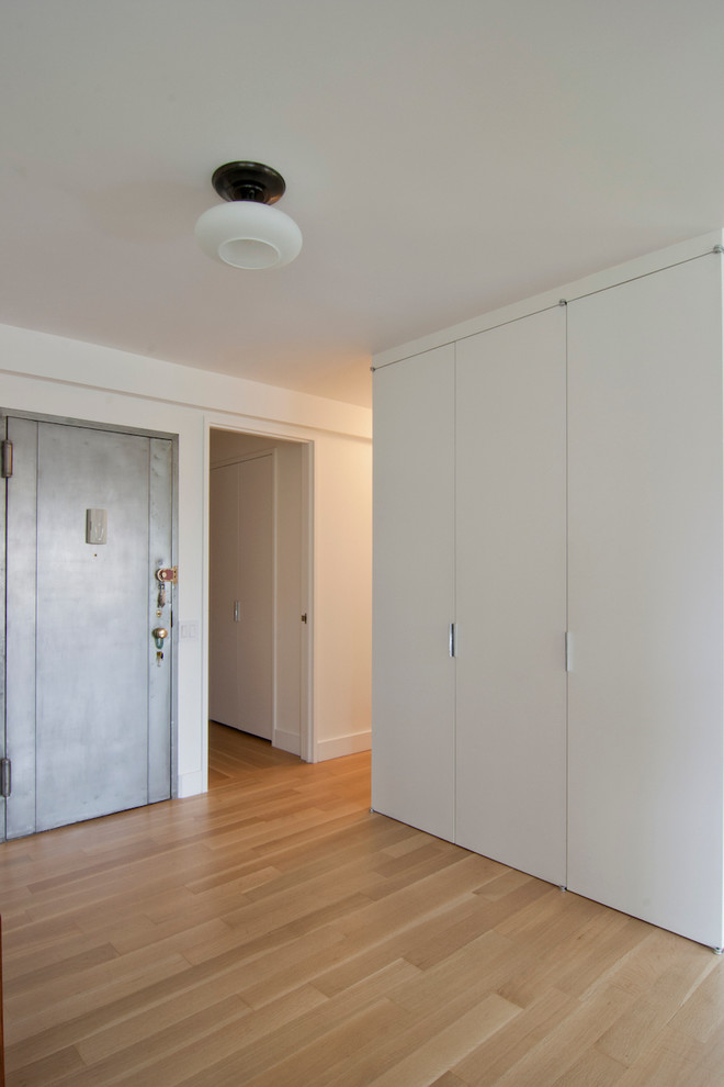 Ejemplo de entrada minimalista pequeña con paredes blancas, suelo de madera clara y suelo beige
