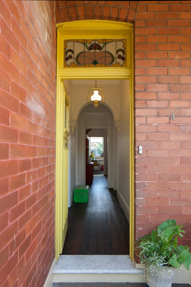 Eklektisk inredning av en liten ingång och ytterdörr, med en gul dörr, en enkeldörr, vita väggar och mörkt trägolv
