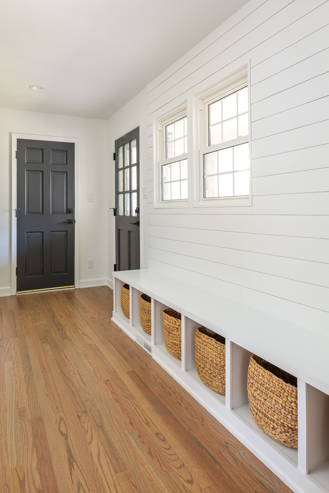 Réalisation d'une grande entrée design avec un vestiaire, un mur blanc, parquet clair, une porte simple, une porte noire et un sol marron.
