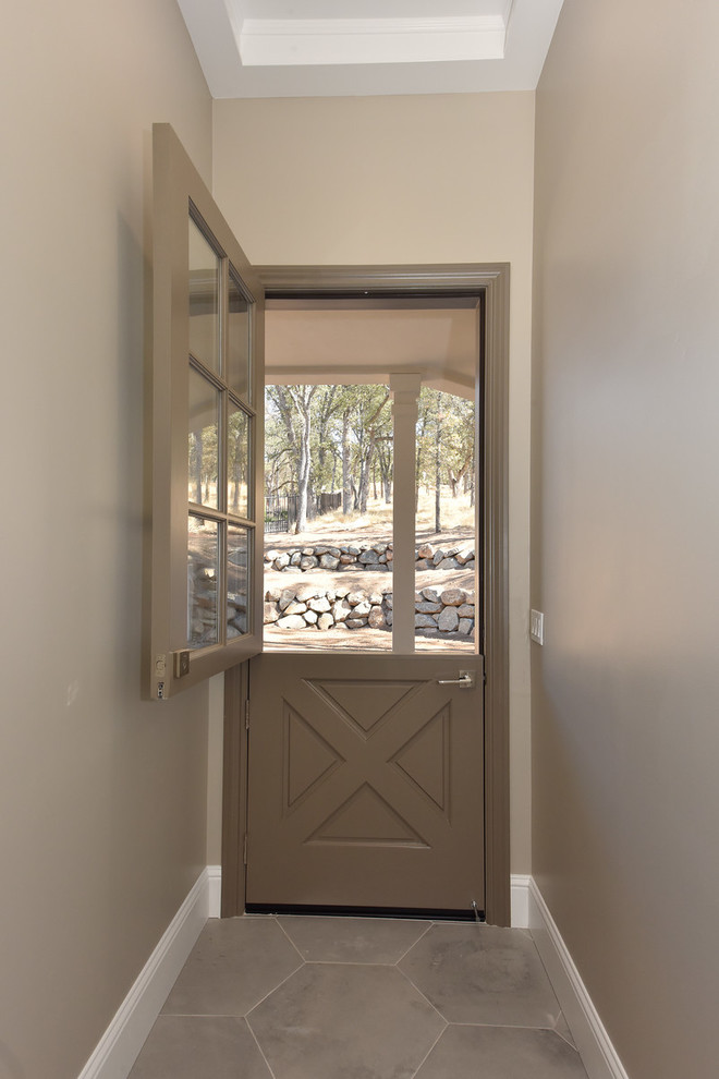 На фото: входная дверь среднего размера в стиле кантри с коричневыми стенами, бетонным полом, голландской входной дверью, коричневой входной дверью и серым полом с