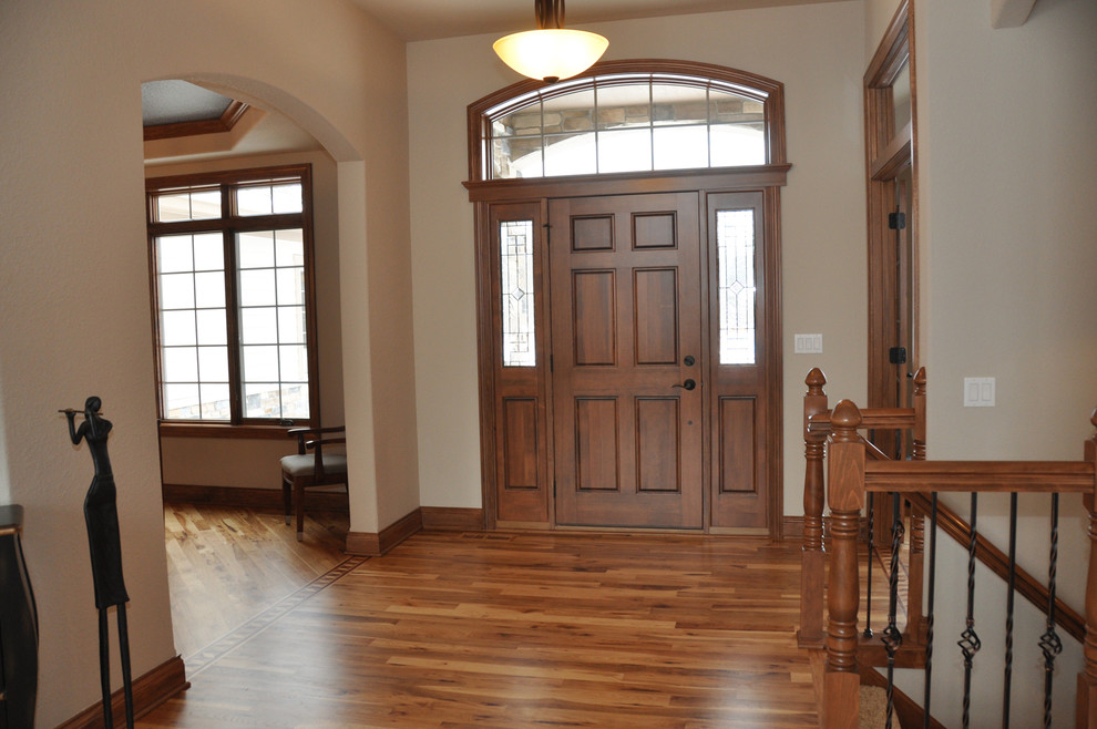 Exemple d'un grand hall d'entrée chic avec un mur beige, un sol en bois brun, une porte simple et une porte en bois brun.