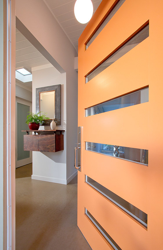 Esempio di una porta d'ingresso moderna con pavimento in cemento, una porta singola e una porta arancione