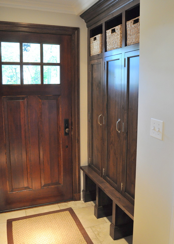 Réalisation d'une entrée tradition de taille moyenne avec un vestiaire, un mur blanc, un sol en calcaire, une porte simple et une porte en bois foncé.