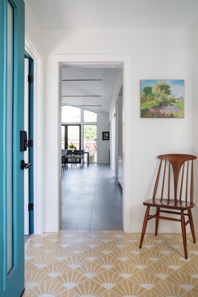Ispirazione per un ingresso minimalista di medie dimensioni con pareti bianche, pavimento in cemento, una porta singola, una porta blu e pavimento giallo