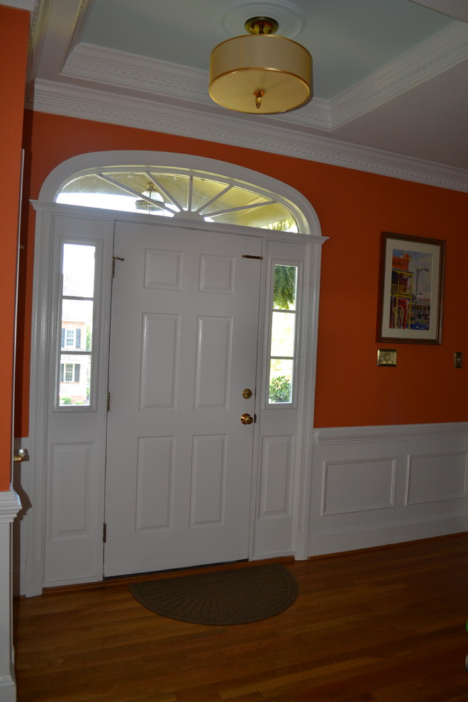 Esempio di un piccolo ingresso tradizionale con pareti arancioni, parquet chiaro, una porta singola e una porta bianca
