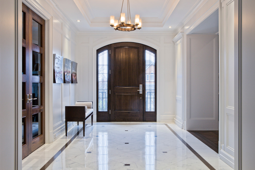 Cette image montre une entrée traditionnelle avec un couloir, un mur blanc, une porte simple, une porte en bois foncé et un sol en marbre.