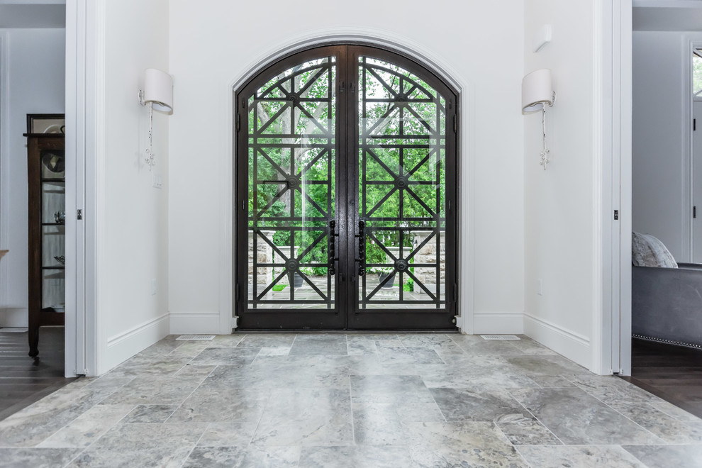 На фото: огромная входная дверь в стиле неоклассика (современная классика) с белыми стенами, мраморным полом, двустворчатой входной дверью, металлической входной дверью и серым полом с