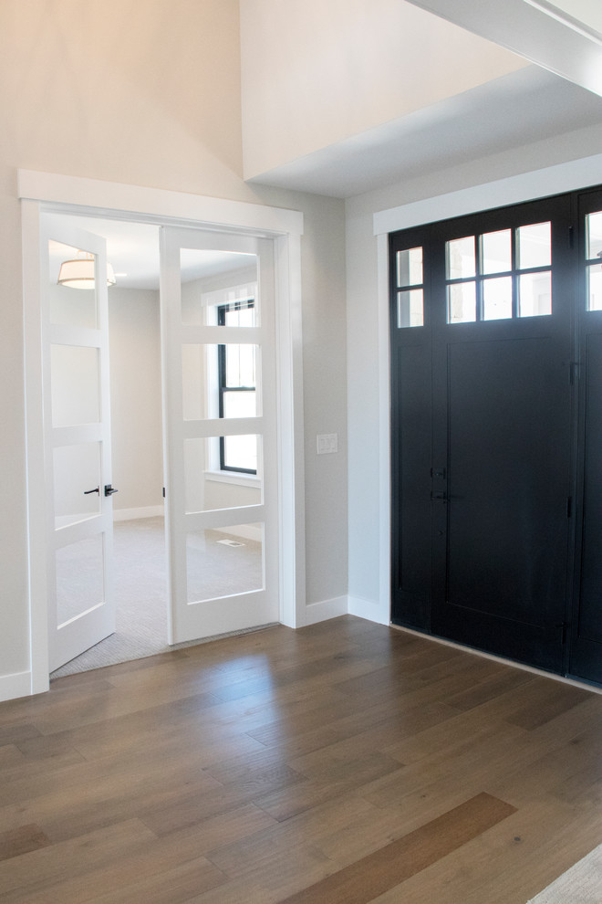 Idée de décoration pour une grande porte d'entrée champêtre avec un mur gris, un sol en bois brun, une porte simple, une porte noire et un sol marron.