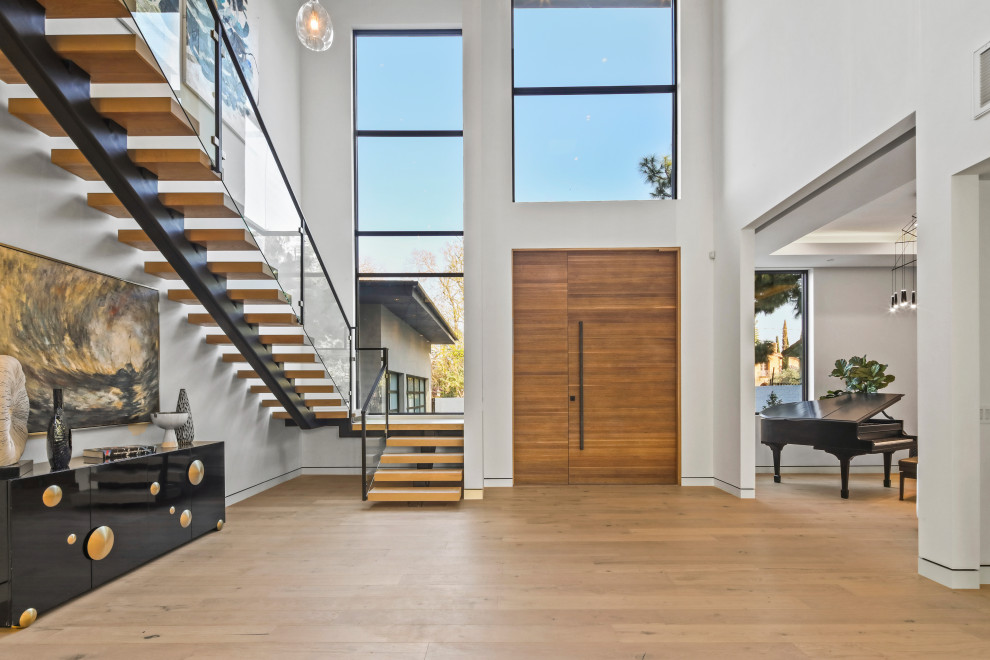 Inspiration for an expansive contemporary front door in Los Angeles with white walls, light hardwood flooring, a single front door, a medium wood front door and beige floors.
