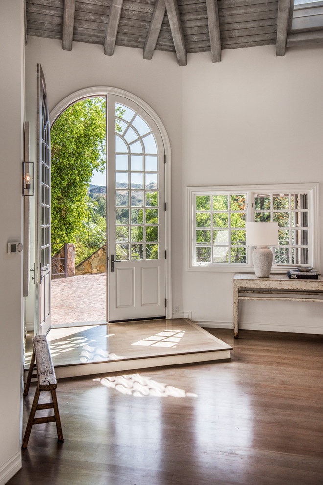 Landhaus Foyer mit weißer Wandfarbe, braunem Holzboden, Doppeltür, Haustür aus Glas und braunem Boden in Los Angeles