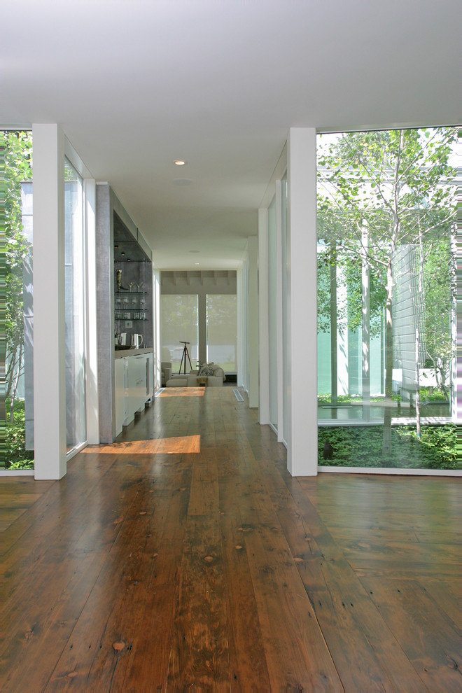 Exemple d'une grande entrée tendance avec un mur blanc, un sol en bois brun, un couloir, une porte simple et une porte en bois foncé.