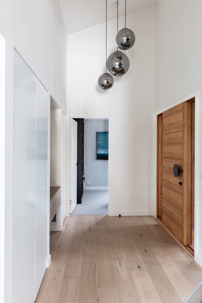 Idee per un ingresso moderno di medie dimensioni con pareti bianche, pavimento in laminato, una porta singola, una porta in legno bruno e pavimento marrone