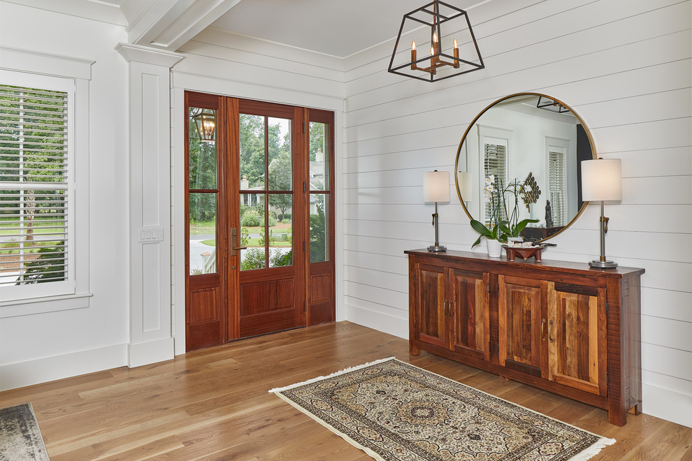 Photo of a medium sized coastal foyer in Charleston with white walls, a single front door, light hardwood flooring, a glass front door and feature lighting.