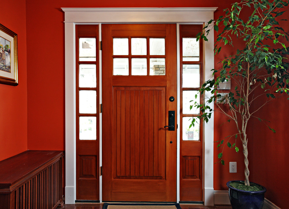 Cette image montre une porte d'entrée traditionnelle de taille moyenne avec un mur rouge, une porte simple, une porte en bois brun et un sol en bois brun.