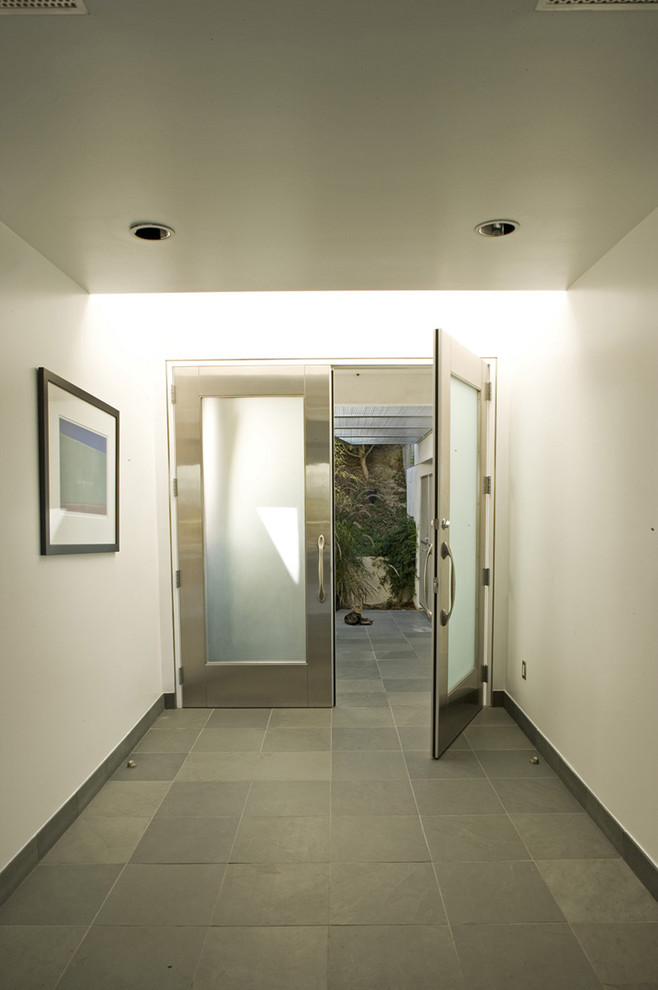 Foto på en funkis entré, med vita väggar, en dubbeldörr, metalldörr och skiffergolv