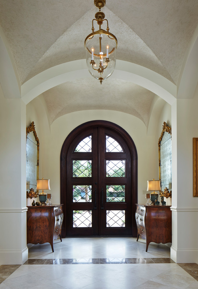 На фото: фойе в классическом стиле с белыми стенами, мраморным полом, двустворчатой входной дверью, входной дверью из темного дерева и белым полом с