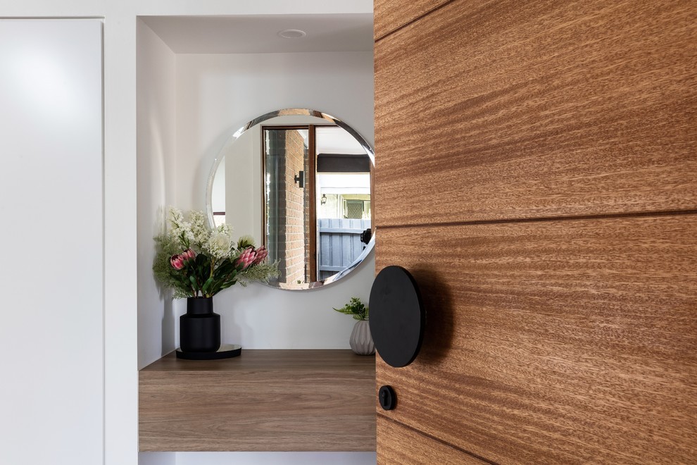 Ispirazione per un ingresso minimalista di medie dimensioni con pareti bianche, pavimento in laminato, una porta singola, una porta in legno bruno e pavimento marrone