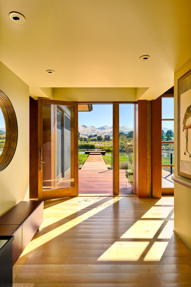 Cette image montre une entrée traditionnelle avec un couloir, un mur beige, parquet clair, une porte simple et une porte en verre.