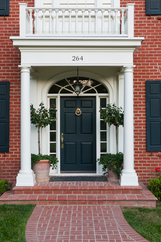 На фото: большая входная дверь в классическом стиле с белыми стенами, кирпичным полом, одностворчатой входной дверью и черной входной дверью