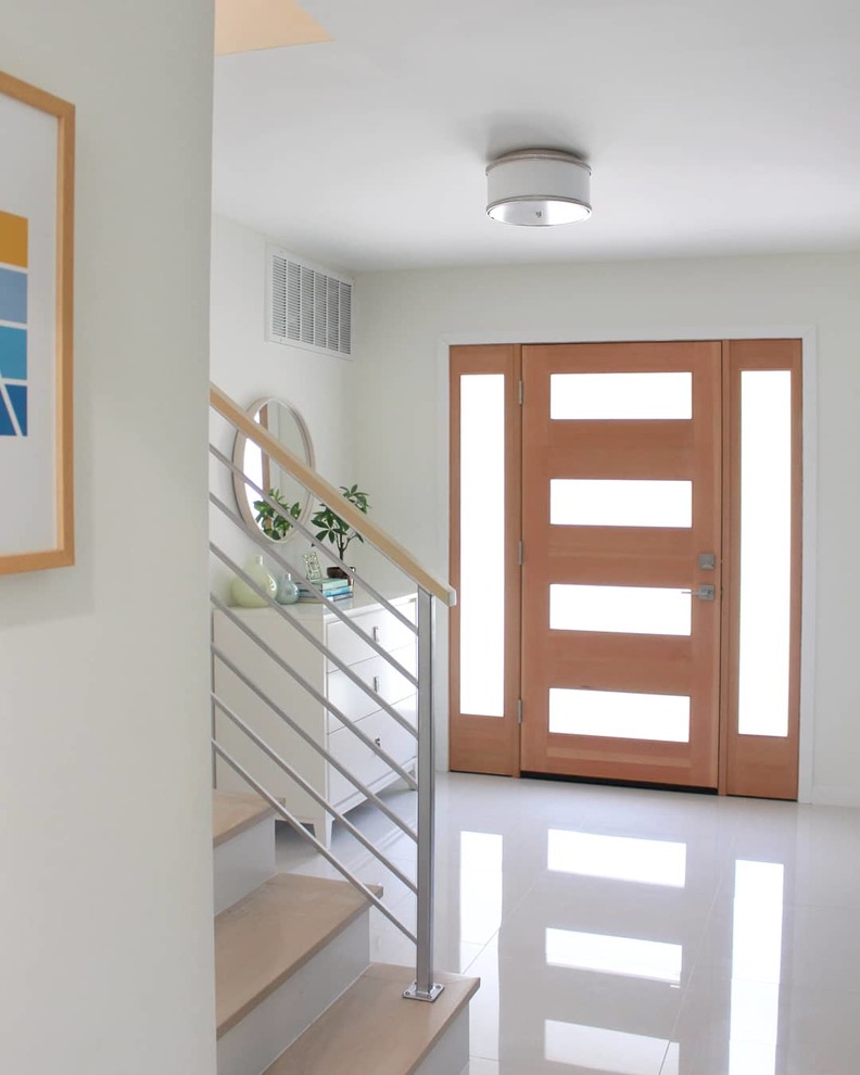 他の地域にあるコンテンポラリースタイルのおしゃれな玄関ドア (白い壁、磁器タイルの床、淡色木目調のドア、白い床) の写真