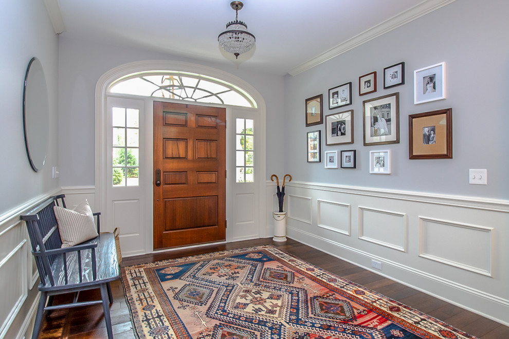 На фото: большая входная дверь в классическом стиле с серыми стенами, паркетным полом среднего тона, одностворчатой входной дверью, входной дверью из дерева среднего тона, коричневым полом и панелями на стенах