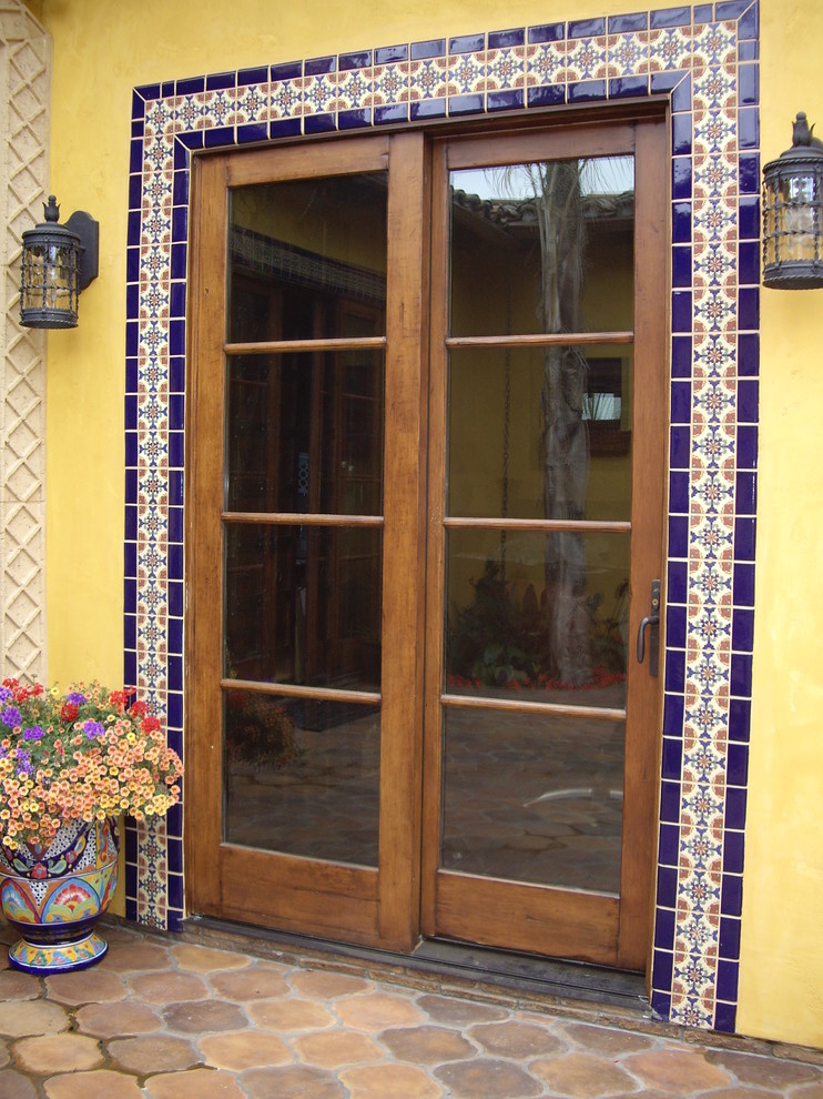 Modelo de puerta principal mediterránea de tamaño medio con paredes amarillas, suelo de baldosas de terracota, puerta doble y puerta de madera clara