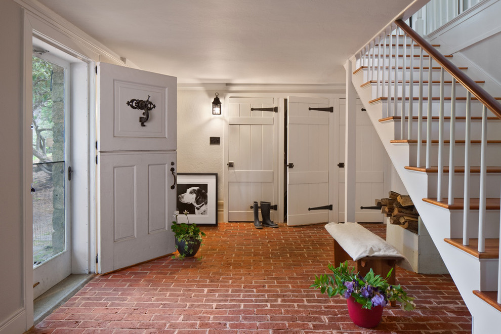Пример оригинального дизайна: фойе в стиле кантри с белыми стенами, кирпичным полом, голландской входной дверью и белой входной дверью