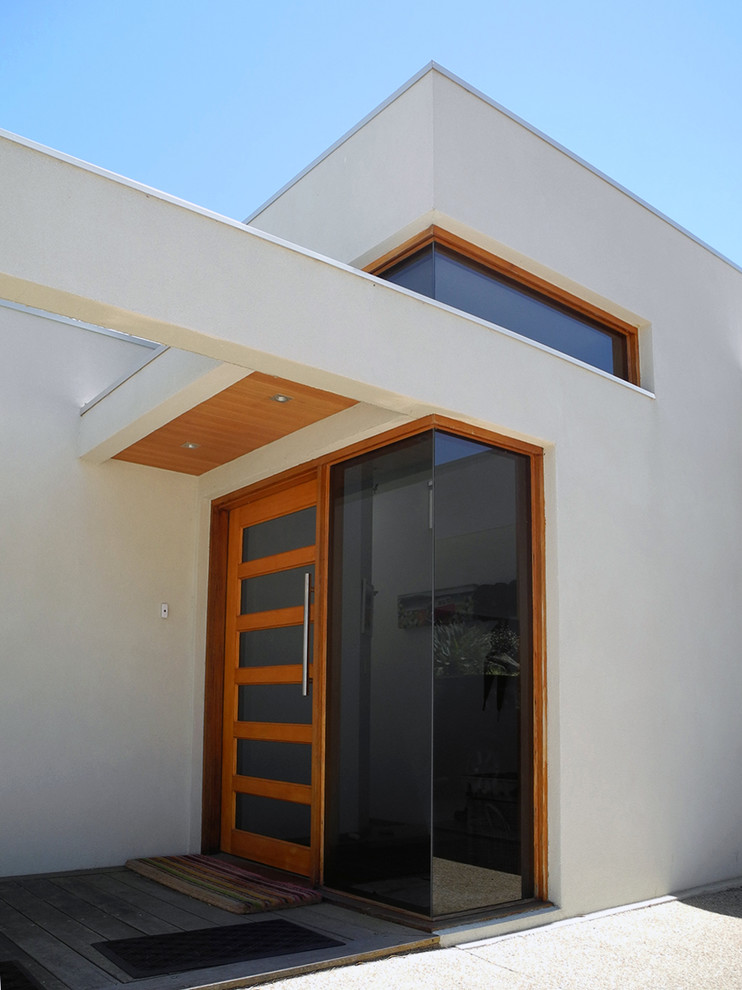Cette photo montre un vestibule moderne de taille moyenne avec un mur blanc, un sol en bois brun, une porte simple, une porte en bois clair et un sol marron.