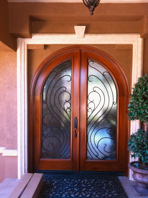 Large mediterranean front door in Orange County with a double front door, a glass front door, brown walls and concrete flooring.