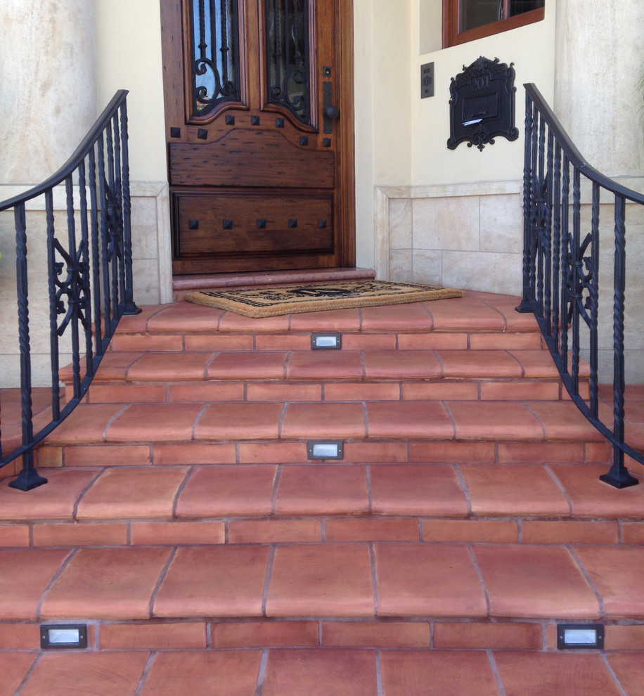 Photo of a large mediterranean entrance in Orange County with beige walls, terracotta flooring, a single front door and a dark wood front door.