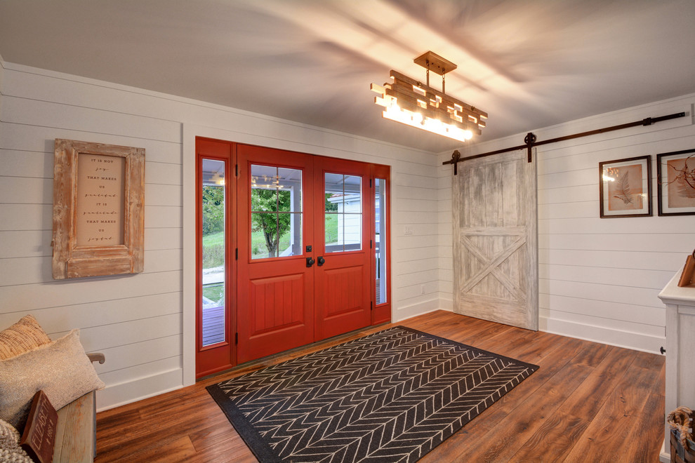Modelo de puerta principal campestre grande con paredes blancas, suelo de madera en tonos medios, puerta doble, puerta roja y suelo marrón