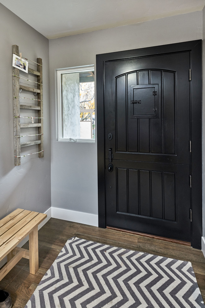 Lantlig inredning av en liten ingång och ytterdörr, med grå väggar, ljust trägolv, en tvådelad stalldörr och en svart dörr