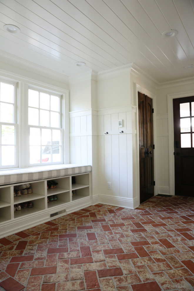 Imagen de vestíbulo posterior de estilo de casa de campo de tamaño medio con paredes blancas, suelo de ladrillo, puerta de madera oscura, suelo rojo, madera y panelado