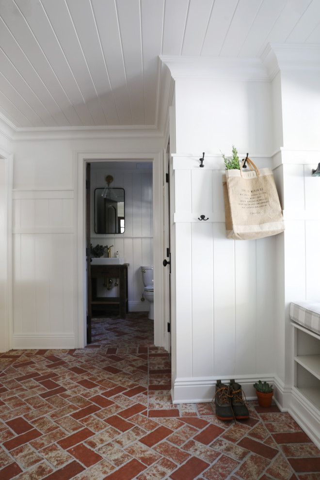 Immagine di un ingresso con anticamera country di medie dimensioni con pareti bianche, pavimento in mattoni, una porta in legno scuro, pavimento rosso, soffitto in legno e pannellatura
