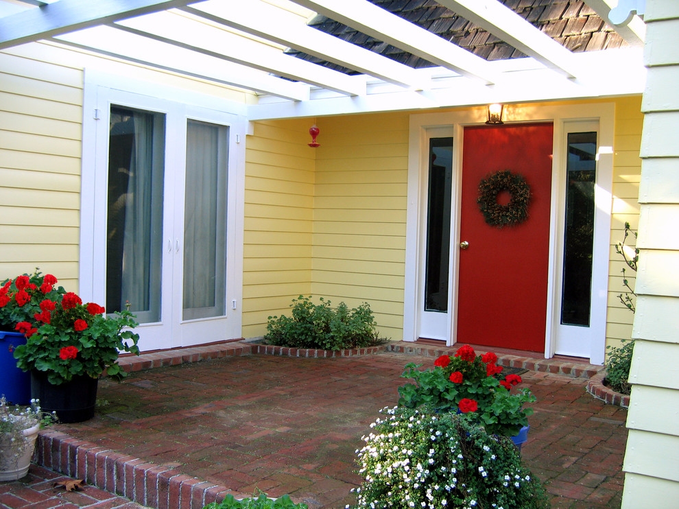 Aménagement d'une très grande porte d'entrée classique avec un mur jaune, une porte simple et une porte rouge.