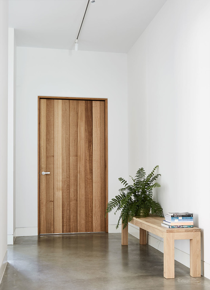 Moderner Eingang mit Betonboden, Einzeltür, hellbrauner Holzhaustür, Korridor, weißer Wandfarbe und grauem Boden in Melbourne