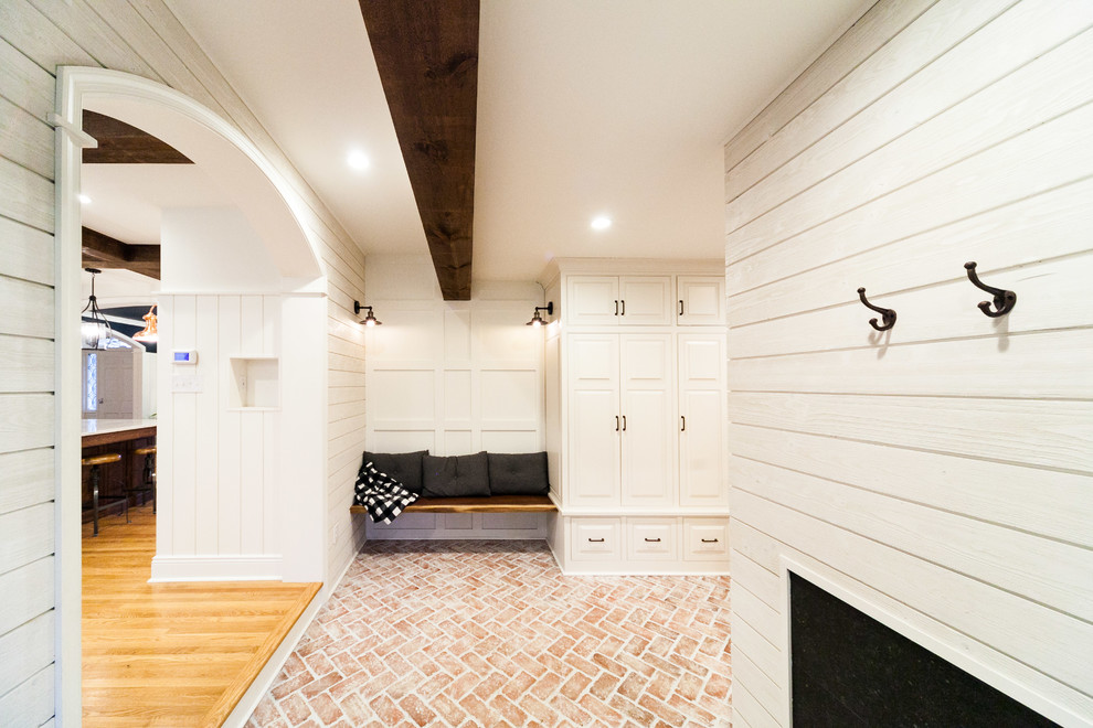 Foto på ett stort lantligt kapprum, med vita väggar, tegelgolv, en enkeldörr, en grå dörr och flerfärgat golv