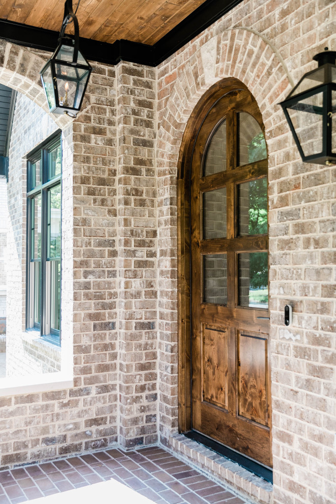 Réalisation d'une grande porte d'entrée tradition avec un sol en brique, une porte simple, une porte en bois brun, un sol marron, un plafond en lambris de bois et un mur en parement de brique.