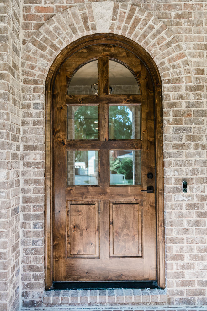 Cette image montre une grande porte d'entrée traditionnelle avec un sol en brique, une porte simple, une porte en bois brun, un sol marron, un plafond en lambris de bois et un mur en parement de brique.